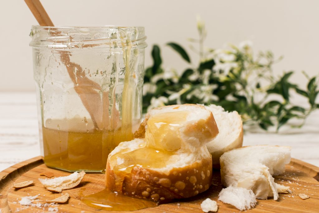 Brot auf einem Holzbrett mit Honig beschmiert und einem Honigglas daneben