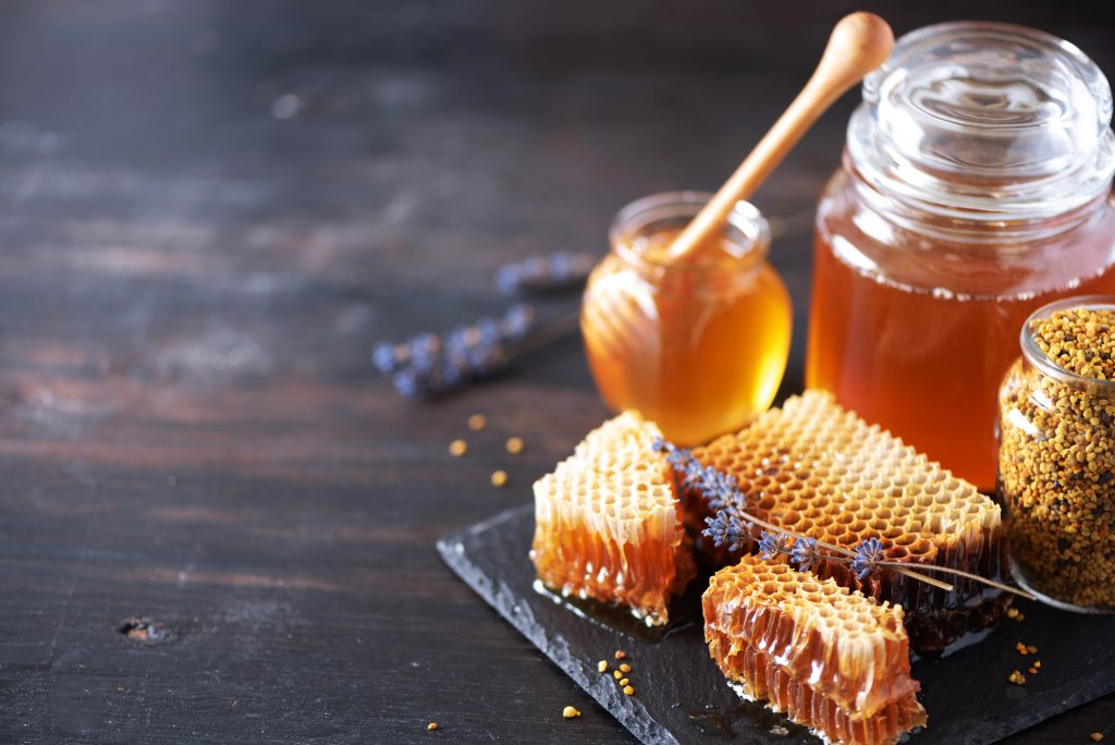Honigglas mit goldfarbenem Honig und Löffel auf Holztisch